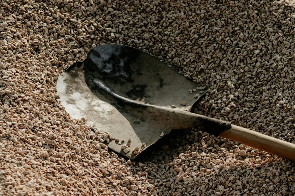 pexels-photo-26925731-26925731 A metal shovel lying on a pile of small pebbles, suggesting outdoor landscaping or construction activities.